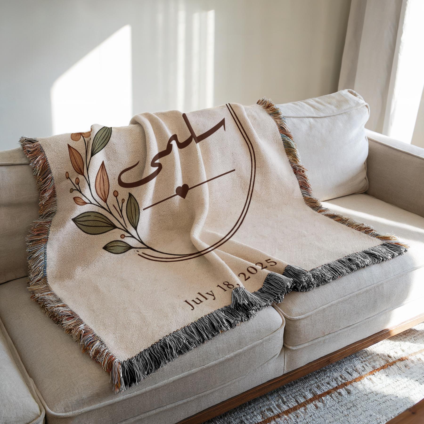 Botanical" personalized blanket draped over a cream sofa in a sunlit room, showcasing the floral design and date while highlighting its tasseled fringe.