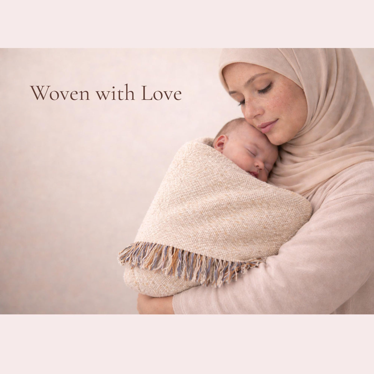 Mother in a beige hijab holding a sleeping baby closely, wrapped partially in the fringed Classic Framed Arabic Calligraphy blanket.