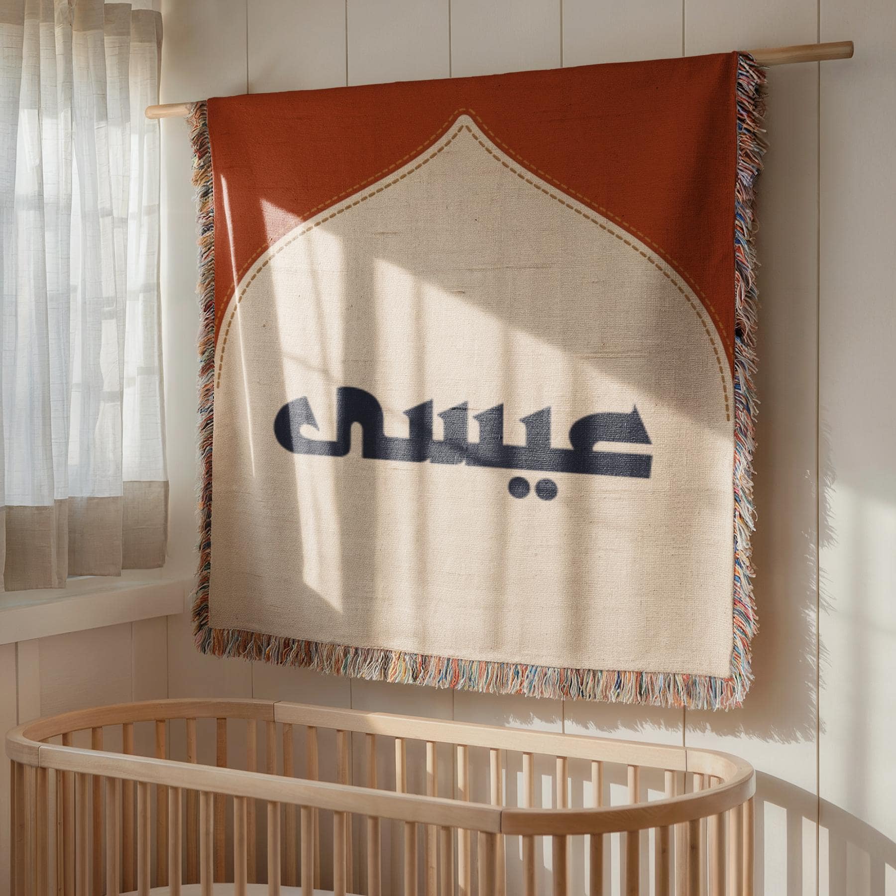 Woven blanket displaying a mosque arch design and Arabic text, hanging on the wall as decorative tapestry above a wooden crib.