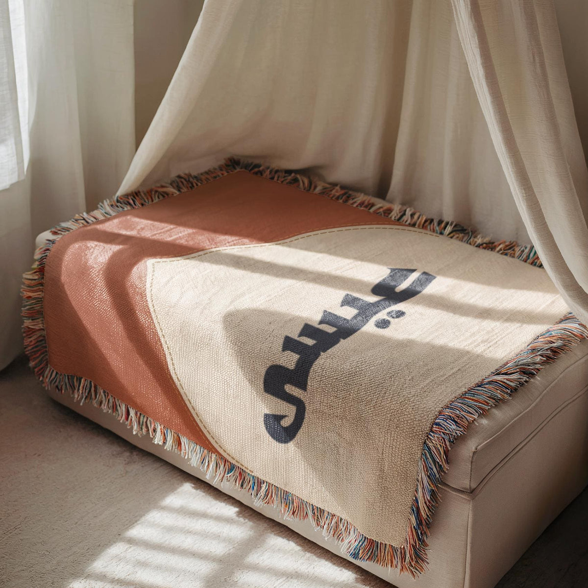 A neutral mosque-themed baby blanket draped over a narrow bench with a tasseled fringe, bathed in soft light.