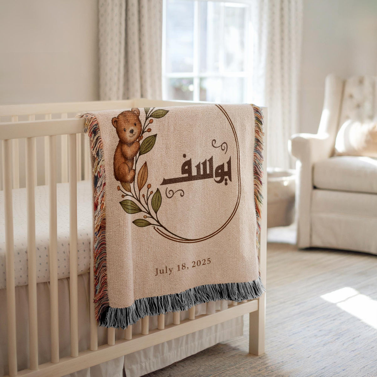 Custom baby blanket showcasing a botanical teddy bear and Arabic name, draped over a white crib beside a window.
