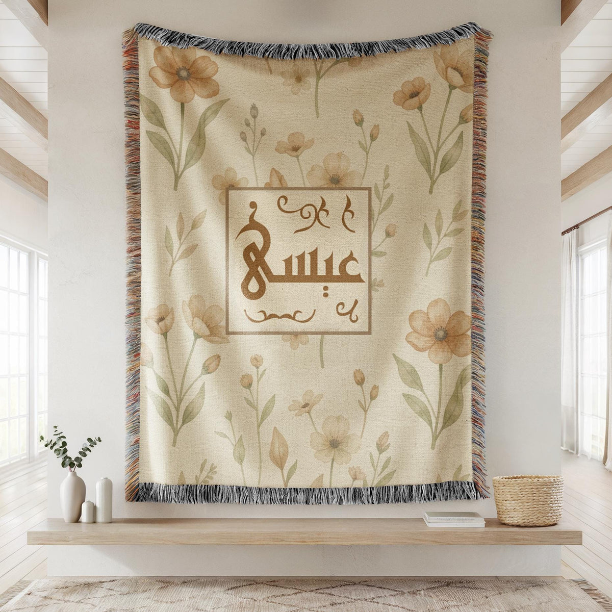 Framed floral pattern baby blanket with custom Arabic name, hanging on the wall as a decorative tapestry above a wooden shelf with a plant.