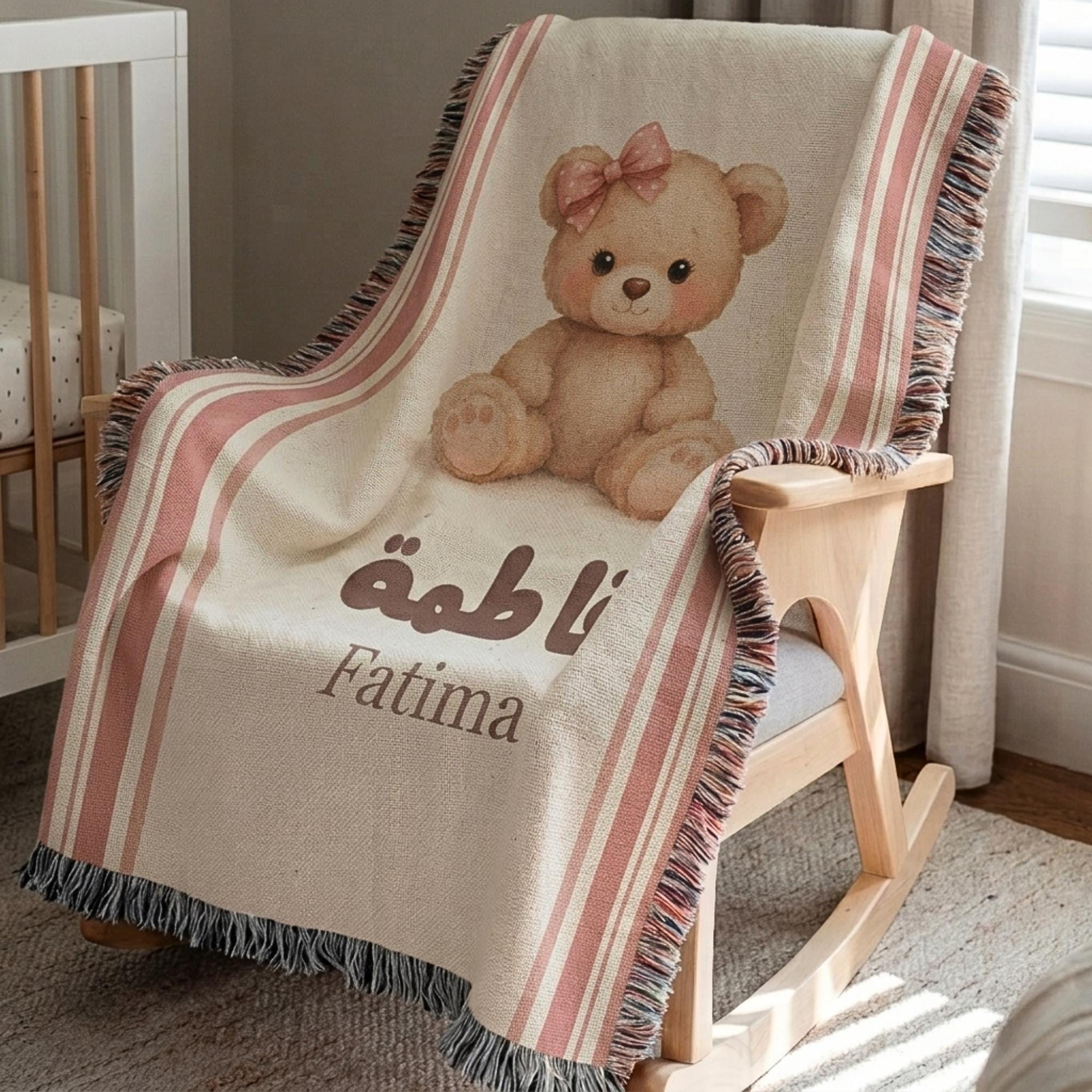 Vintage bear patterned baby blanket draped over a wooden rocking chair, highlighting the blush pink stripes, teddy bear illustration, and fringed edges.